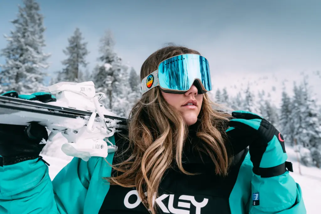 A woman gearing up for ski boot testing, holding a pair of women's ski boots.