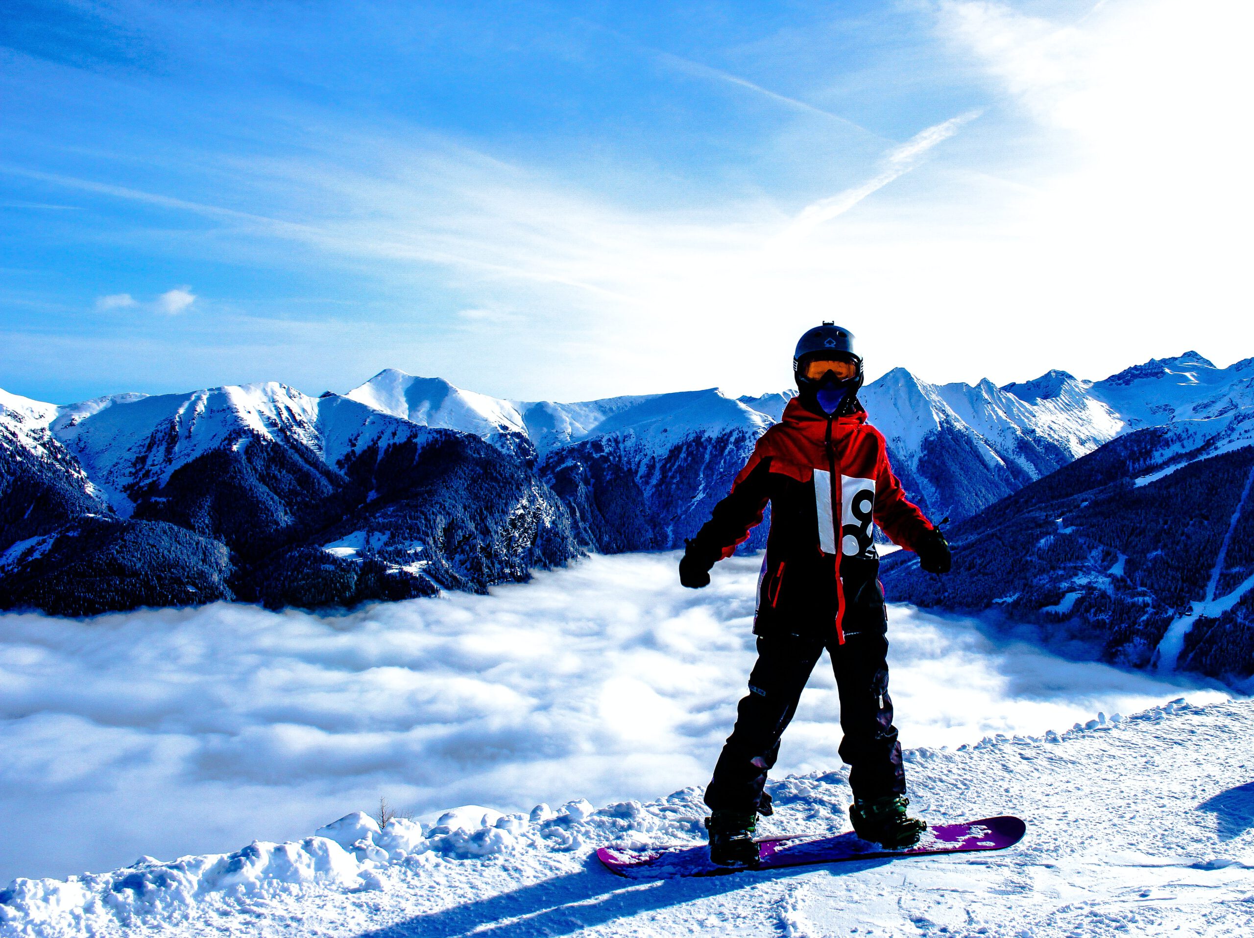 Snowboarder standing in front of a huge mountain, dressed in a stylish mid-layer jacket.