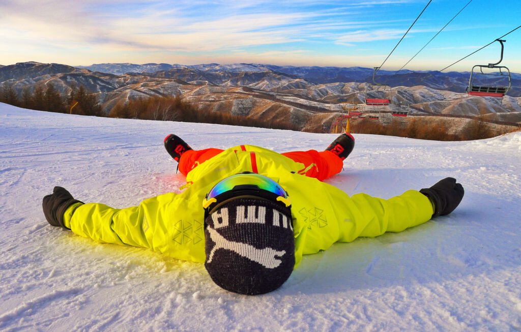 A man in a bright yellow mid-layer jacket lying in the snow.